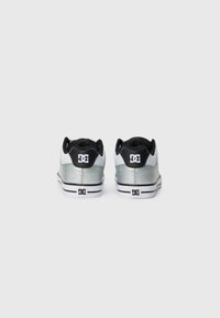 Un par de zapatillas bajas DC en plata y blanco vistas desde atrás, con cuellos acolchados negros y el logo de DC en el talón y la suela.