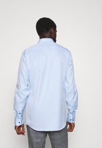 Lichtblauw overhemd met een button-down kraag, lange mouwen en zwarte knoopaccenten op de manchetten, een gladde textuur en een gebogen zoom.