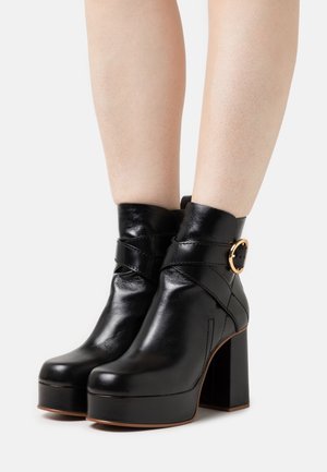 Černé kožené kotníkové boty s kulatou špičkou, masivním vysokým podpatkem a ozdobnou zlatou sponou na boku. Hladká textura.