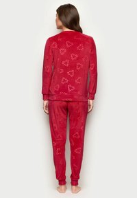 Rød fleece pyjamas sæt bestående af en langærmet trøje og bukser, begge med et hjerte mønster og blød, tekstureret overflade.