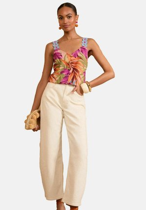 Floral-patterned sleeveless top with blue decorative straps paired with high-waisted cream wide-leg pants, accessorized with a woven bag.