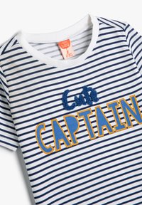 Valkoinen ja tummansininen raidoitettu lyhythihainen paita, jossa on "Söpö KAPTEENI" -teksti oranssina ja sinisenä, teksturoitu brodeeraus sekä ommeltu pyöreä pääntie.