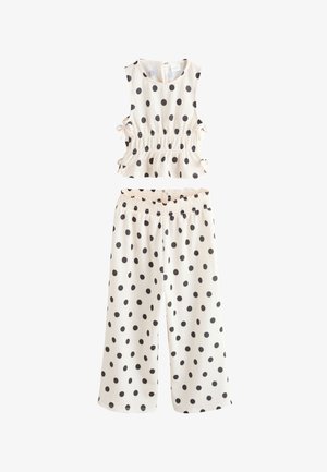 Wit mouwloos crop top en broek met wijde pijpen met zwarte polkadots en zijstrikjes aan het topje.