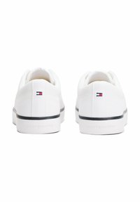 White canvas sneakers with a textured surface, featuring a black rubber sole and a small logo accent on the back.
