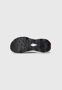Semelle de chaussure en caoutchouc noir avec un motif texturé comportant des clous hexagonaux et un accent rouge près du talon, sur fond blanc.