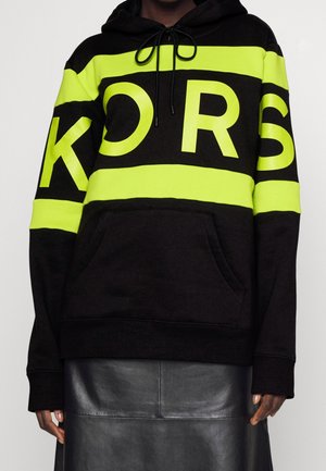 Hoodie nero realizzato in materiale morbido, con strisce verde neon audaci e scritta "KORS". Include un cappuccio con lacci e tasca frontale.