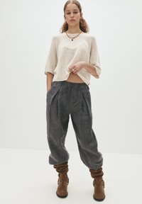 Hellbeige gestricktes Cropped-Top mit kurzen Ärmeln, kombiniert mit lockeren, dunkelgrauen gefalteten Hosen und braunen, lässigen Stiefeletten. Einfach und strukturiert.