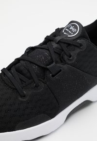 Sneakers Nike neri con una parte superiore testurizzata e design in rete, punta rotonda e suola in gomma bianca. I lacci sono neri e integrati in modo ordinato.