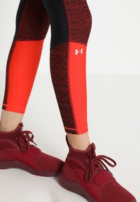 Legginsy w czerwono-czarny wzór o gładkiej fakturze, połączone z czerwonymi butami sportowymi z wyściółką w okolicy kostki i sznurowadłami.