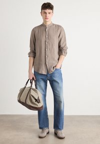 Linnen overhemd met knopen in taupe, relaxte pasvorm; blauwe denim jeans; beige sport-tas met bruine accenten; grijze schoenen. Eenvoudig ontwerp en textuur.