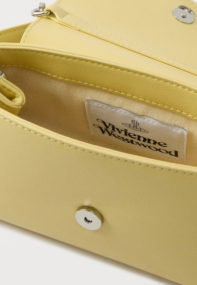 Εσωτερικό κίτρινης τσάντας από τεχνητό δέρμα με κούμπωμα με πατώντας. Διαθέτει υφασμάτινη ετικέτα με το όνομα της μάρκας, λεία υφή και στρογγυλεμένες άκρες.