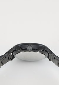 Montre noire en métal avec un cadran rond, deux boutons latéraux et une lunette polie. Le bracelet présente un design à maillons pour un aspect robuste.