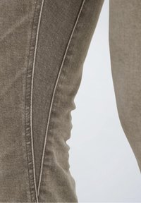 Gros plan sur un tissu en denim marron montrant une couture latérale détaillée et une texture avec de légères rides.