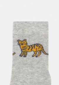 Graue Baumwollesocken mit einem aufgedruckten Design eines gelb-schwarz gestreiften Tigers, mit einer strukturierten Oberfläche und einem gerippten Bund.