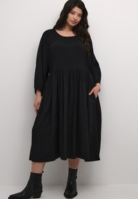 Black midi dress with a scoop neckline, long sleeves, and textured diamond pattern. Features a gathered waist and side pockets. Paired with black ankle boots.