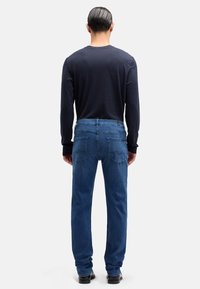 Granatowa koszula z długim rękawem w połączeniu z niebieskimi dżinsami. Dżinsy mają tylne kieszenie z ozdobnym przeszyciem; koszula ma dopasowane rękawy i okrągły dekolt.