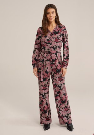 Floral jumpsuit in black with pink and cream flowers. Long sleeves, V-neck, cinched waist, and wide-leg pants. Smooth texture with a tie belt.