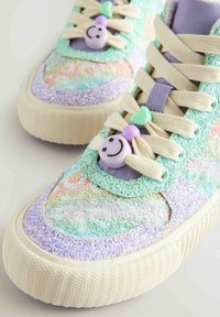 Błyszczące pastelowe sneakersy z teksturowaną miętową cholewką, lawendowymi akcentami i zabawnymi plastikowymi zawieszkami. Gumowa podeszwa z wzorzystym bieżnikiem.