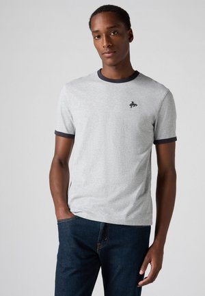 Grijze T-shirt met korte mouwen en een ronde halslijn, marineblauwe afwerking en een klein zwart logo op de borst; gecombineerd met donkerblauwe jeans.
