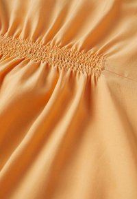Tissu orange avec des coutures élastiques froncées créant des volants uniformément espacés au centre.