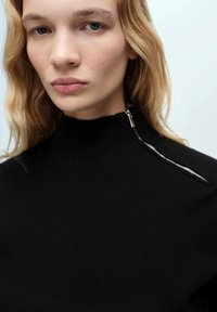 Maglione nero a collo alto con zip sulla spalla sinistra, realizzato in un tessuto morbido e con un design aderente.