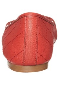 Ballerines en cuir rouge avec une texture matelassée, présentant un dos arrondi et une semelle plate couleur marron clair. Petits accents de couture visibles.