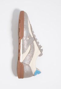 Nizki superge z srebrnimi bleščečimi prekrivanji, bež tkanina, belo vezalke, gumijasti podplat in modra zanka na peti z besedilom znamke.