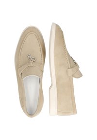 Scarpe slip-on in suede beige con punta arrotondata, fiocco decorativo e accentuazione in metallo con logo, e suola in gomma bianca. Texture liscia.