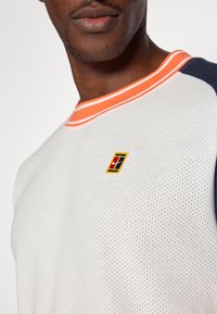 Λευκό κοντομάνικο πουκάμισο από διχτυωτό υλικό με πορτοκαλί ριγέ γιακά, διαθέ�τει ένα πολύχρωμο κεντητό λογότυπο στο στήθος. Ο σχεδιασμός περιλαμβάνει ναυτικές λεπτομέρειες.