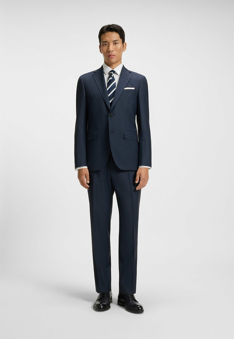 Mörkblå kostym med en strukturerad mönster, en vit skjorta och en randig slips. Har en enkel knappstängning och en slim fit-design.