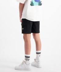 Zwarte cargoshorts met twee zijzakken, gecombineerd met witte sneakers en gestreepte sokken. Het shirt heeft een grafisch ontwerp in levendige kleuren.