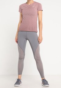Camiseta deportiva rosa claro de manga corta con una textura sutil, combinada con leggins gris ajustados que tienen paneles de malla y costuras ergonómicas.