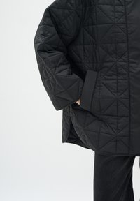 Giacca imbottita nera con motivo a rombi, maniche ampie e tasche laterali. Realizzata in un materiale liscio e leggero.
