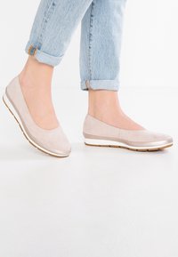 Beige semišové baleríny s kulatou špičkou, jemným šitím a bílou gumovou podrážkou, spárované s vyhrnutými světlými džíny.