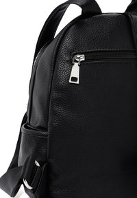 Sac à dos en cuir noir avec une texture grainée, quincaillerie en argent, poche zippée à l'avant et bretelles ajustables. Design compact et arrondi.