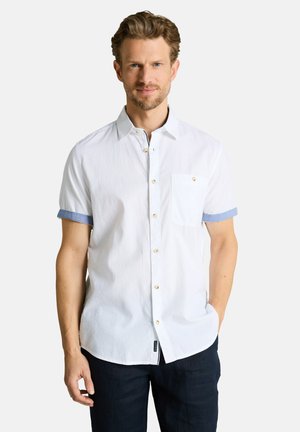 Man with short brown hair and beard wearing a white short-sleeve button-up shirt with blue cuff accents and dark pants, standing against white background.