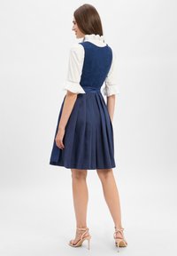 Navy blue dress with a fitted bodice and pleated skirt. Features a textured fabric, ruffled white collar, and a soft sash at the waist.