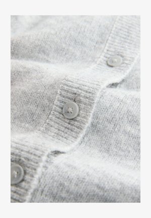 Šviesiai pilkas kardiganas, pagamintas iš minkštos mezginio medžiagos, pasižymintis akordeono tekstūra ir apvaliais mygtukais tokios pat spalvos.