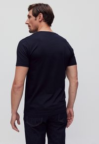 Navyblauwe katoenen t-shirt met korte mouwen, ronde halslijn en een gladde textuur, gezien van achteren. Gecombineerd met donkere jeans.