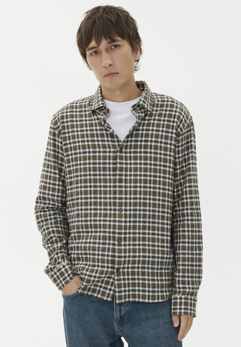 Brązowa i biała koszula w kratę z długimi rękawami, z kołnierzykiem, z brązowymi guzikami z przodu. Nosi się ją na białej koszulce z okrągłym dekoltem.