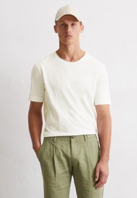 Helles Cremet-Shirt mit kurzen Ärmeln und rundem Ausschnitt, kombiniert mit olivgrünen, gefalteten Hosen. Glatte Textur, lässige Passform.