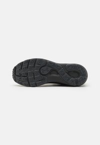Semelle de chaussure de sport noire avec caoutchouc texturé, présentant des motifs de traction multidirectionnels et un logo Under Armour.