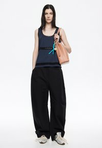 Canottiera navy con dettagli in pizzo, pantaloni neri a gamba larga e sneakers argentati. Una borsa a tracolla rosa chiaro con accessori a forma di portachiavi è tenuta in mano.