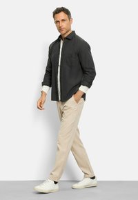 Black button-up shirt with a single chest pocket, layered over a white shirt, paired with cream corduroy trousers and white sneakers.