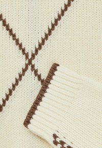 Adīts džemperis krēmkrāsā ar dimanta rakstu un brūnām akcentēm. Iespējo ribotas aproces un auduma tekstūras variācijas.