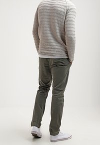 Szary sweter z teksturą w poziome paski, w połączeniu z zielonymi bawełnianymi spodniami i białymi sneakersami, o luźnym kroju i swobodnym stylu.