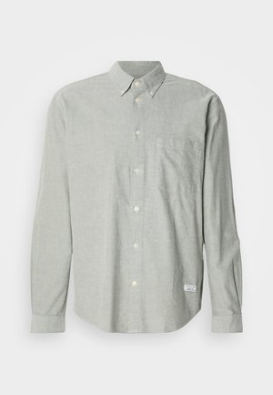 Camicia grigia chiara con bottoni realizzata in tessuto strutturato. Presenta un colletto, maniche lunghe, una tasca sul petto e un'etichetta in basso a sinistra.