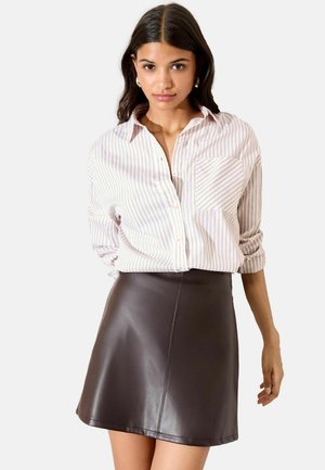 Brown faux leather mini skirt paired with a light striped button-up shirt, featuring rolled sleeves and a front pocket detail.