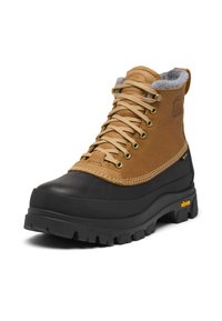 Botte à cheville en cuir marron avec un embout en caoutchouc noir, une doublure grise, des œillets dorés et une semelle Vibram texturée pour l'adhérence.