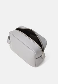 Trousse de toilette en cuir gris avec une forme rectangulaire, un extérieur texturé, une fermeture éclair sur le dessus et une poignée latérale pour un transport facile.
